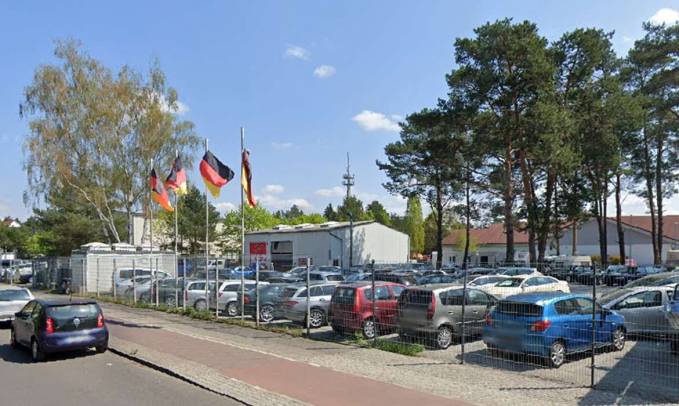 Der Verkaufsplatz an der Müggellandstraße mit parkenden Fahrzeugen und Kiefern im Hintergrund
